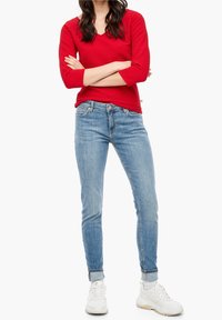 Röd ribbad långärmad topp med V-ringning och trekvartsärmar, i kombination med ljusblå jeans i skinny-modell och vita sneakers.