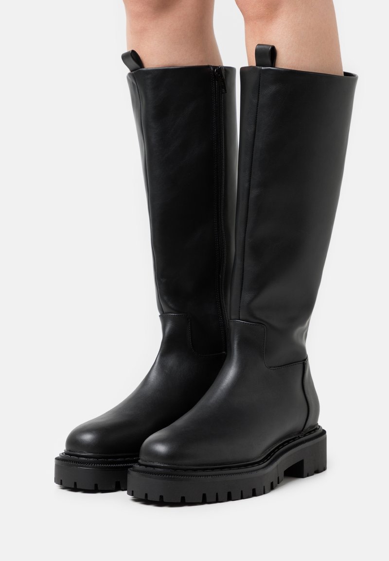 Stivali neri in pelle al ginocchio con una texture liscia, zip laterale e suola spessa e scolpita. Presentano una punta arrotondata e un'apposita linguetta per la calzata.