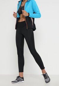 Lightweight, hooded blue jacket with black accents, paired with black high-waisted leggings. Textured black athletic shoes complete the outfit.