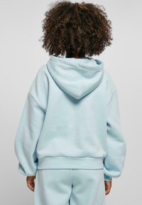 Light blue hoodie made of soft material, featuring a large hood, dropped shoulders, and ribbed cuffs. See a portion of matching pants.