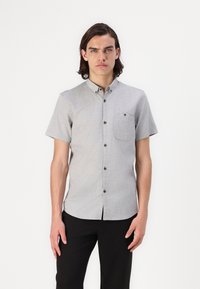 Korte mouw, geknoopte blouse met kraag in lichtgrijze stof. Heeft een borstzak en donkere knopen, een zachte textuur en strakke lijnen.