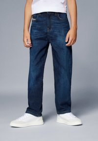 Jeans in denim blu con taglio dritto, leggero sbiadimento e design standard a cinque tasche. Indossati con sneakers bianche.