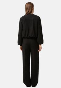 Czarna kurtka bomberka z krótkim krojem i elastycznym pasem, zestawiona z wysokim stanem, szerokimi czarnymi spodniami o gładkiej fakturze.