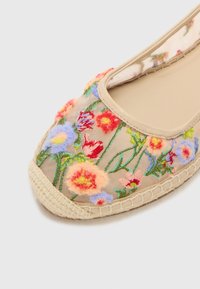 Bestickte Espadrille mit flachem Absatz, die ein oberes Gewebe in Beige mit bunten Blumenmustern, eine abgerundete Zehenpartie und einen Juteschuhrand aufweist.