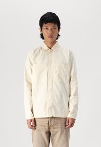Light beige long-sleeve shirt with a collared neck, two chest pockets, and a straight cut, made from a textured cotton fabric.