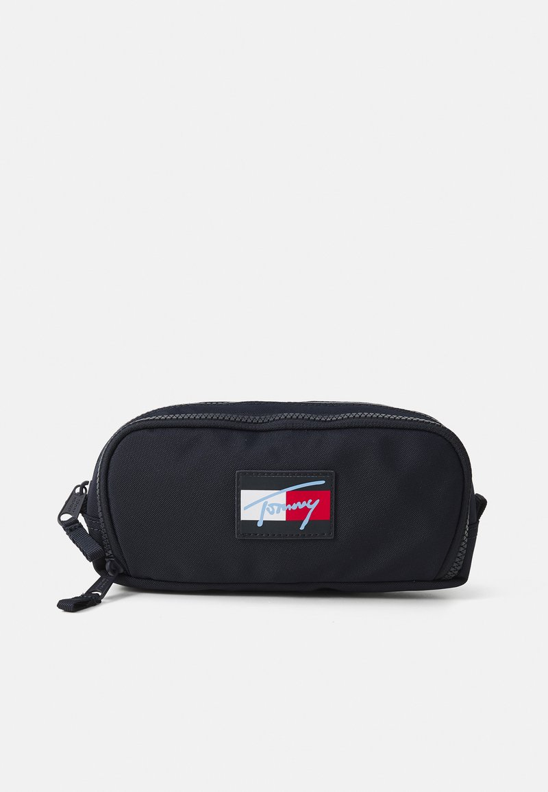 Schwarzes Nylonetui mit einem Reißverschluss, das ein Tommy-Logoetikett in Blau, Rot und Weiß aufweist. Kompakte rechteckige Form, glatte Textur.
