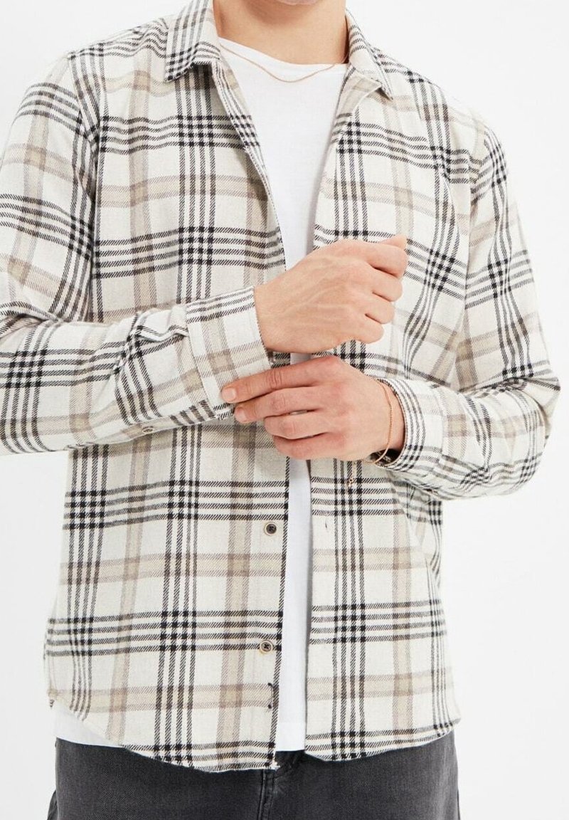 Camicia a quadri in tonalità crema, nera e beige. Realizzata in tessuto morbido con chiusura a bottoni, taschino sul petto e maniche lunghe.