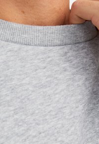 Lichtgrijze sweatshirtkraag met een geribbelde textuur, die een zachte stof toont. Zichtbare naden bij de halslijn.
