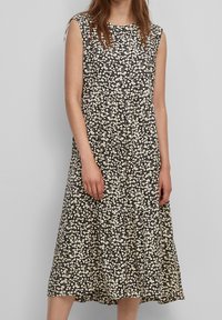 Vestido negro sin mangas con un patrón floral blanco, que presenta un escote redondo y un dobladillo en capas flotante que llega hasta la mitad de la pantorrilla.