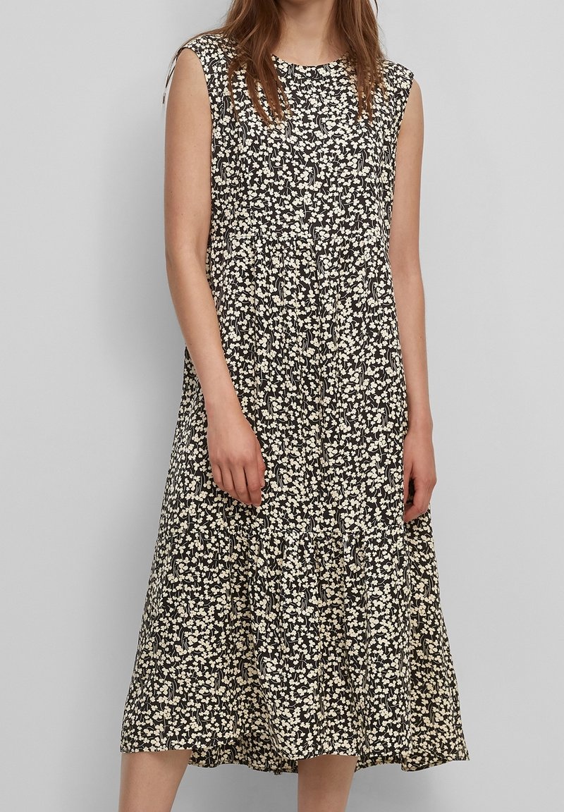 Vestido negro sin mangas con un patrón floral blanco, que presenta un escote redondo y un dobladillo en capas flotante que llega hasta la mitad de la pantorrilla.
