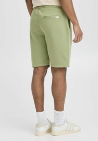 Lys grønne shorts lavet af blødt stof med elastisk talje og en baglomme. Båret med hvide sneakers og hvide ankelstrømper.