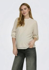 Suéter texturizado de cor creme, com mangas três quartos e decote redondo, combinado com jeans soltos de cor cinza escuro.