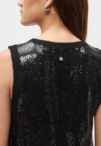 Μαύρο αμάνικο τοπ με μπροστινό μέρος από παγιέτες και πλεκτή πλάτη, με στρογγυλή λαιμόκοψη και μικρή μεταλλική λεπτομέρεια λογότυπου στο λαιμό.