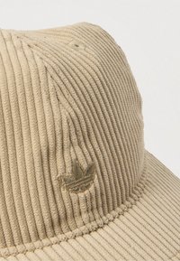 Beige bøttehatt i kordfløyel med vertikal rillet tekstur, med en subtil brodert logo i en mørkere nyanse.