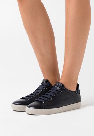 Navy blue leather sneakers with a smooth finish, textile laces, and a textured heel detail. Cream rubber sole with subtle pattern design.