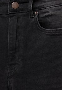 Gros plan sur un jean en denim noir montrant la poche avant, la boucle de ceinture, le bouton en métal et les détails de couture.