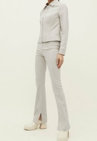 Lysegrå, tætsiddende lynlåstrøje med krave og matchende vide bukser med sideslids, stylet med chunky hvide plateau sko.