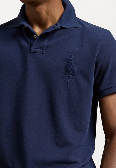 Polo de Navy con tejido texturizado, mangas cortas y una tapeta de tres botones. Un logotipo bordado de un jugador de polo es visible en el pecho.