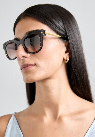 Lunettes de soleil écaille de tortue noires avec une monture carrée, des accents en métal doré et des verres dégradés. Texture lisse avec des bords géométriques bien définis.