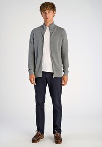Grå zip-up cardigan med en texturerad design, tillsammans med en vit t-shirt, marinblå byxor och bruna loafers.