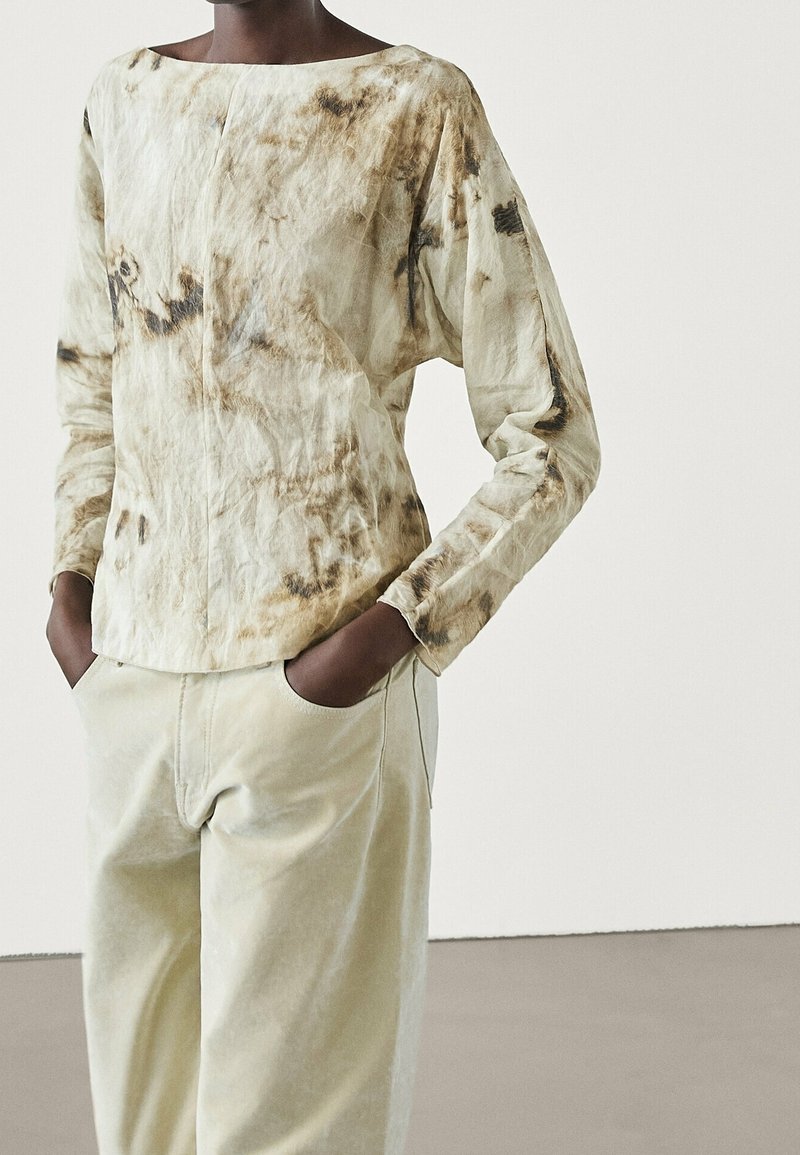 Haut à manches longues en beige clair avec un motif tie-dye marron, doté d'un col bateau et d'une coupe décontractée, associé à un pantalon de couleur crème.