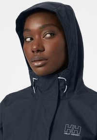 Navy waterproof jacket with a hood, featuring adjustable drawstring and logo on the chest, made from smooth, durable fabric.