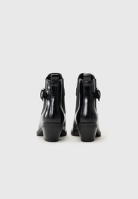 Botas de tobillo de cuero negro con un acabado texturizado, que presentan un pequeño tacón y un detalle de hebilla lateral. Diseño liso y elegante.