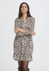 Brūns un krēmkrāsas rakstains kleita ar V veida kakla izgriezumu, garām piedurknēm un brīvu piegriezumu. Izgatavota no viegla auduma ar gludu tekstūru.