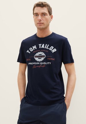 Navyblaue Baumwoll-T-Shirt mit einem grafischen Druck von "Tom Tailor" in Weiß und Rot, rundem Ausschnitt und kurzen Ärmeln.