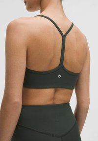 Sujetador deportivo de color verde oscuro con un diseño de espaldas cruzadas, fabricado en un tejido suave. Presenta un pequeño logotipo cerca de la parte central de la espalda.