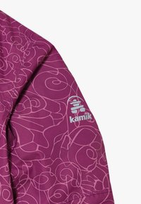 Veste violette avec un motif de lignes tourbillonnantes, avec un logo sur la manche. Fabriquée en tissu lisse et texturé.