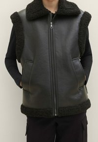 Schwarze Lederweste mit einem Kunstfellkragen, verfügt über Seitentaschen und einen Frontreißverschluss, kontrastreiche Texturen in einem minimalistischen Design.