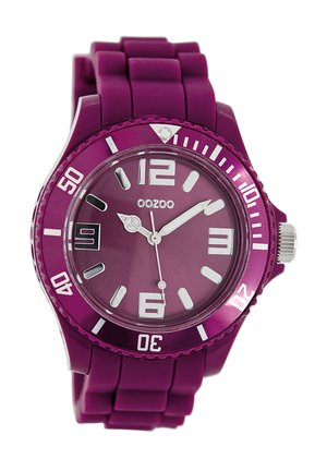 Montre en silicone violet avec un boîtier rond, des index d'heure blancs contrastants et un bracelet texturé. Présente une couronne imposante et un design minimaliste.