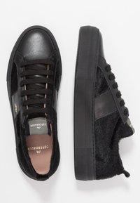 Svarta sneakers med en kombination av läder och strukturerad tyg, rund tå, platt sula och platta snörningar med gulddetaljer.