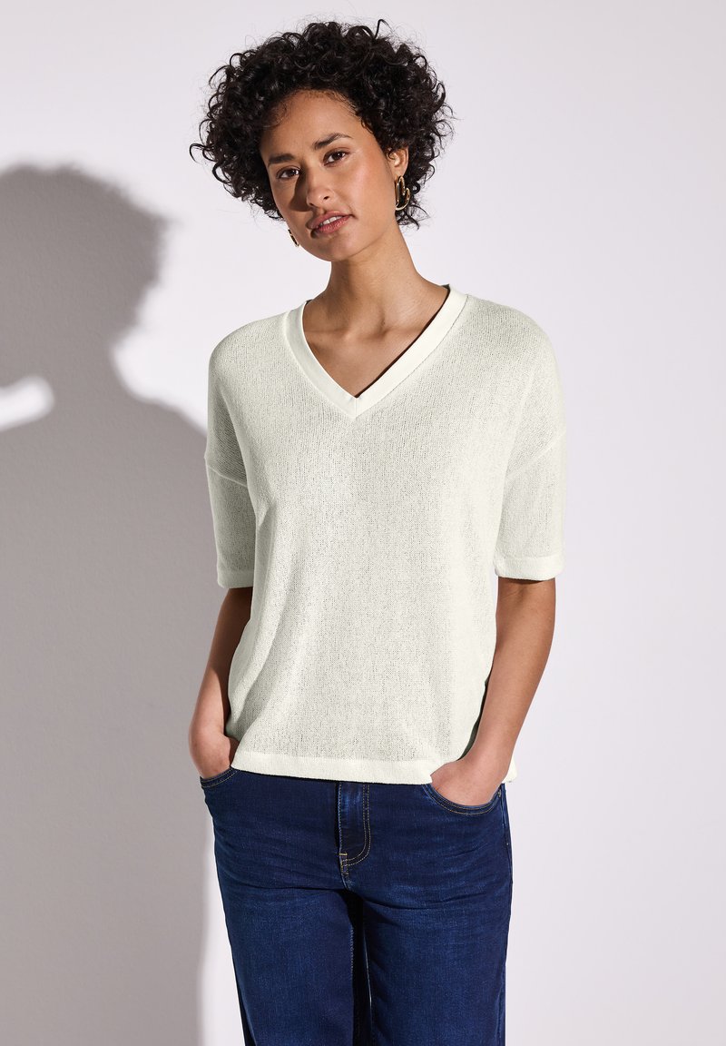 Lichtbeige V-hals top met korte mouwen, gemaakt van tekstiel met structuur. Gecombineerd met donkerblauwe denim jeans. Eenvoudig ontwerp, relaxte pasvorm.