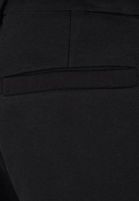Tejido negro elástico con una textura suave, que presenta un sutil detalle de bolsillo trasero. El diseño es sencillo y ajustado, ideal para el uso casual.