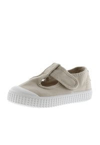 Scarpa di tela beige con cinturino in velcro, punta rotonda e suola in gomma bianca. Presenta dettagli traforati sui lati. Tessuto testurizzato.