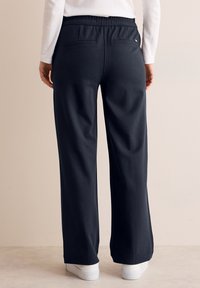 Marinefarbene, locker sitzende Hosen mit einem Kordelzugbund und Gesäßtaschen. Hergestellt aus weichem Stoff mit glatter Textur und geradem Bein.