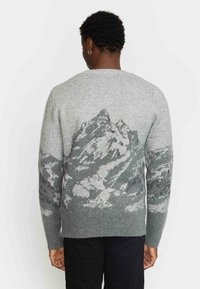 Grauer Strickpullover mit einem Gebirgslandschaftsdesign in dunkleren Grautönen auf der Rückseite. Die Textur wirkt weich, mit gerippten Bündchen.