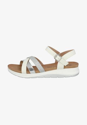 Weiße Sandale mit metallisch silbernen Akzenten, ausgestattet mit überkreuzten Riemen, einem Schnallenverschluss, einem gepolsterten Fußbett und einer weißen Gummisohle.