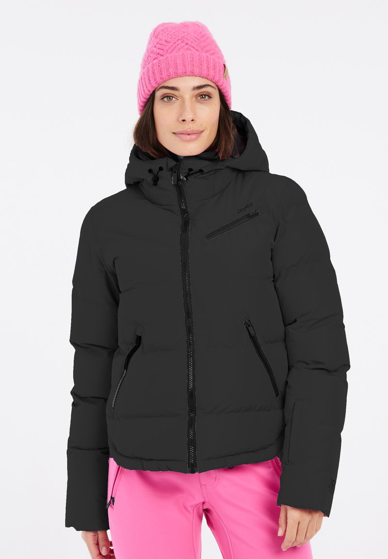 Schwarze Daunenjacke mit einem Reißverschluss vorne, zwei seitlichen Taschen und einer verstellbaren Kapuze. Getragen mit einer leuchtend rosa gestrickten Mütze.