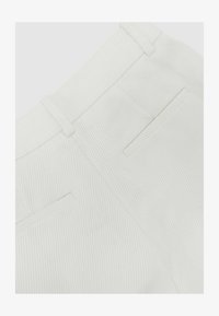Primer plano de pantalones de tela blanca texturizada que muestran la pretina, las trabillas y dos bolsillos traseros de ojal.