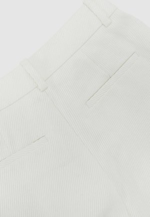 Nærbillede af hvide teksturerede stofbukser med synlig linning, bæltestropper og to baglommer med skrå åbning.