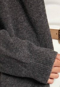 Mörkgrå, mjuk ulltröja med ribbade ärmar och en avslappnad design, med en närbild på den texturerade tyget och ärmdetaljer.