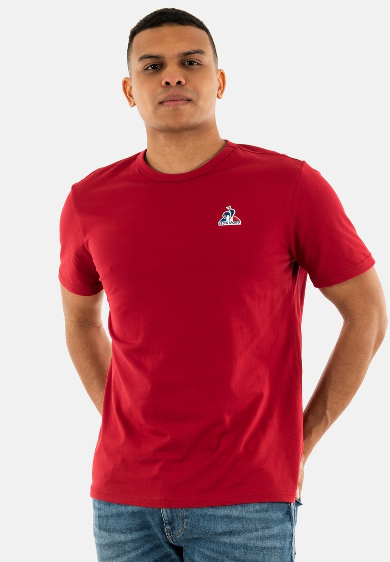 Camiseta de algodón roja con mangas cortas, escote redondo y pequeño logo azul en el lado izquierdo del pecho. Textura suave, corte casual.