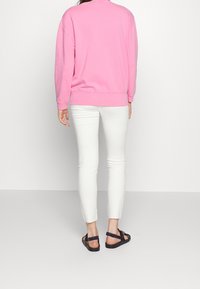 Pink sweatshirt with ribbed cuffs and hem, paired with white skinny jeans and black strappy sandals, viewed from the back.