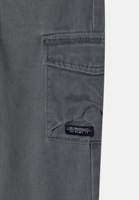 Grijze stof met een gestructureerd oppervlak, met een zijvak en een label waarop "BY NOME IT." staat. Eenvoudig, functioneel ontwerp.