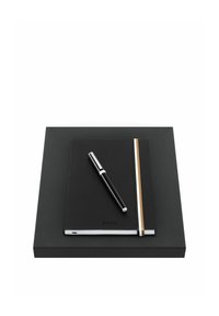 Cahier noir avec bande élastique et stylo argenté posé sur une boîte rectangulaire noire sur fond blanc.