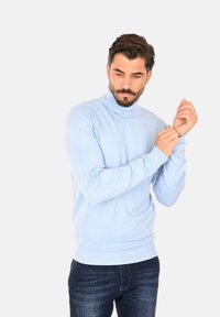 Maglione a collo alto azzurro chiaro realizzato in morbido tessuto, con maniche aderenti e polsini a costine. Abbinato a jeans blu scuro.