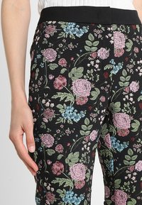 Svarta mönstrade byxor med ett blommönster som har rosa och blå blommor samt gröna blad. Midjan är i ett solid svart och strukturerad.